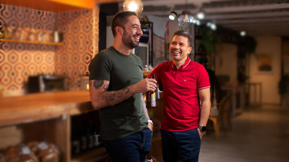 Dos amigos compartiendo un momento en un café, vistiendo camisetas Apoštol QC